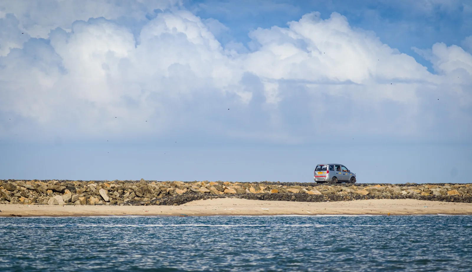 A coastal road with a bus beside blue water and clouds at Dhanushkodi